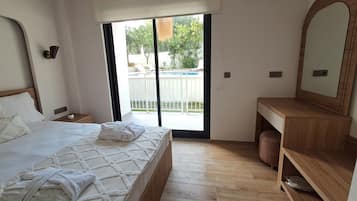Un dormitorio con cama, una mesita de noche de madera, un aparador de madera, un espejo grande y una puerta corrediza de vidrio que da a un espacio al aire libre.