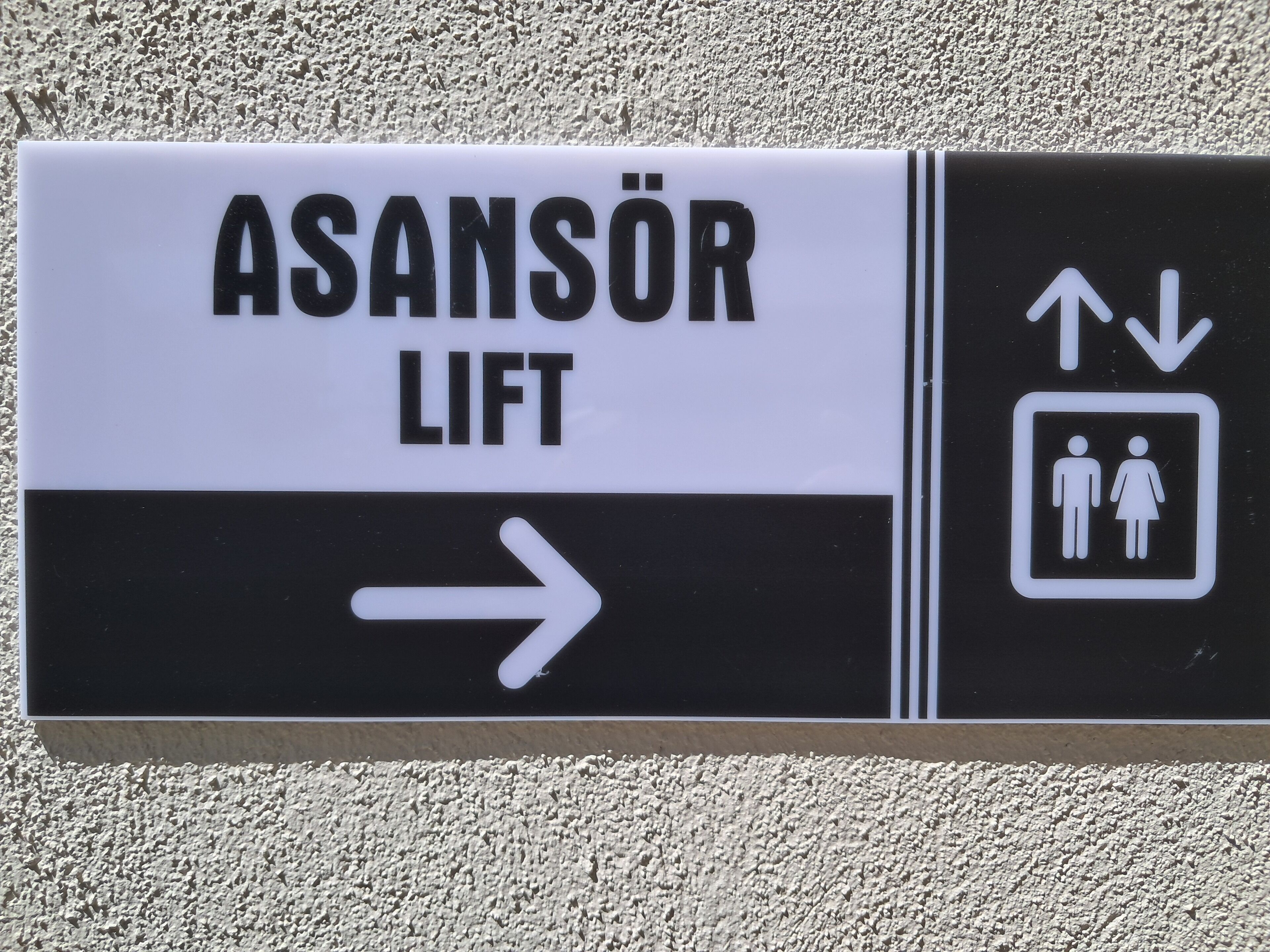 A directional sign with "ASANSÖR LIFT" and an arrow pointing right, indicating the location of a lift.