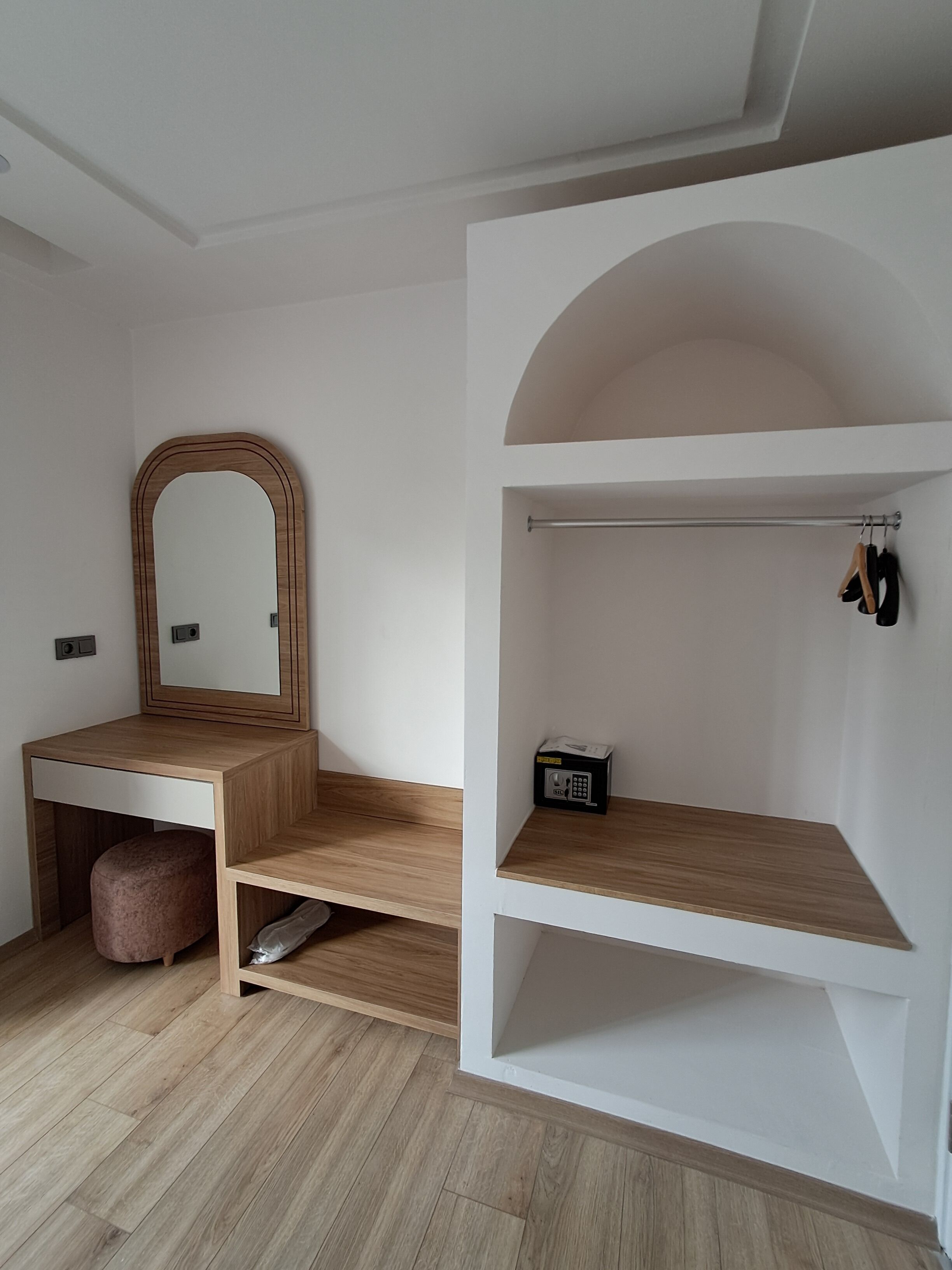 A minimalist room with a wooden desk, a large mirror, and a white shelving unit.