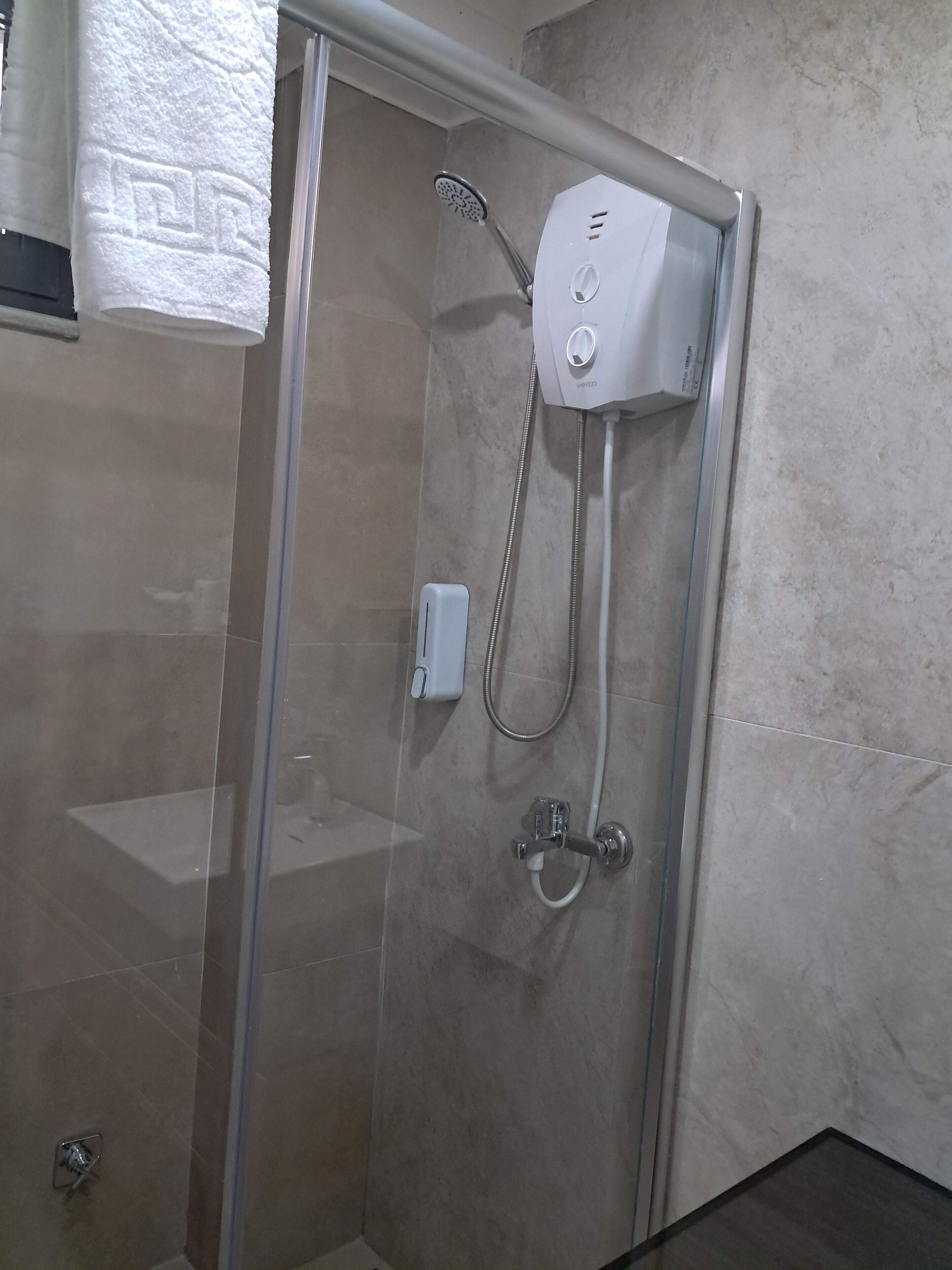 Ducha con cerramiento de vidrio, cabezal de ducha manual y panel de control en la pared.
