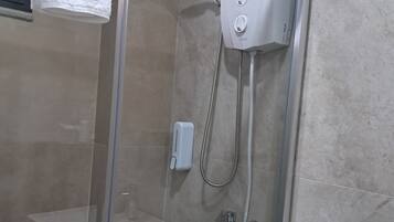 Ducha con cerramiento de vidrio, cabezal de ducha manual y panel de control en la pared.