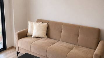 A beige sofa with two pillows, a black coffee table with a plant, and a window with blinds.