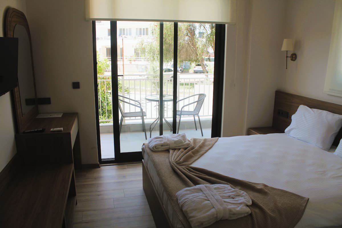 A hotel room with a large bed, a desk, a chair, and a balcony with a view of the street.