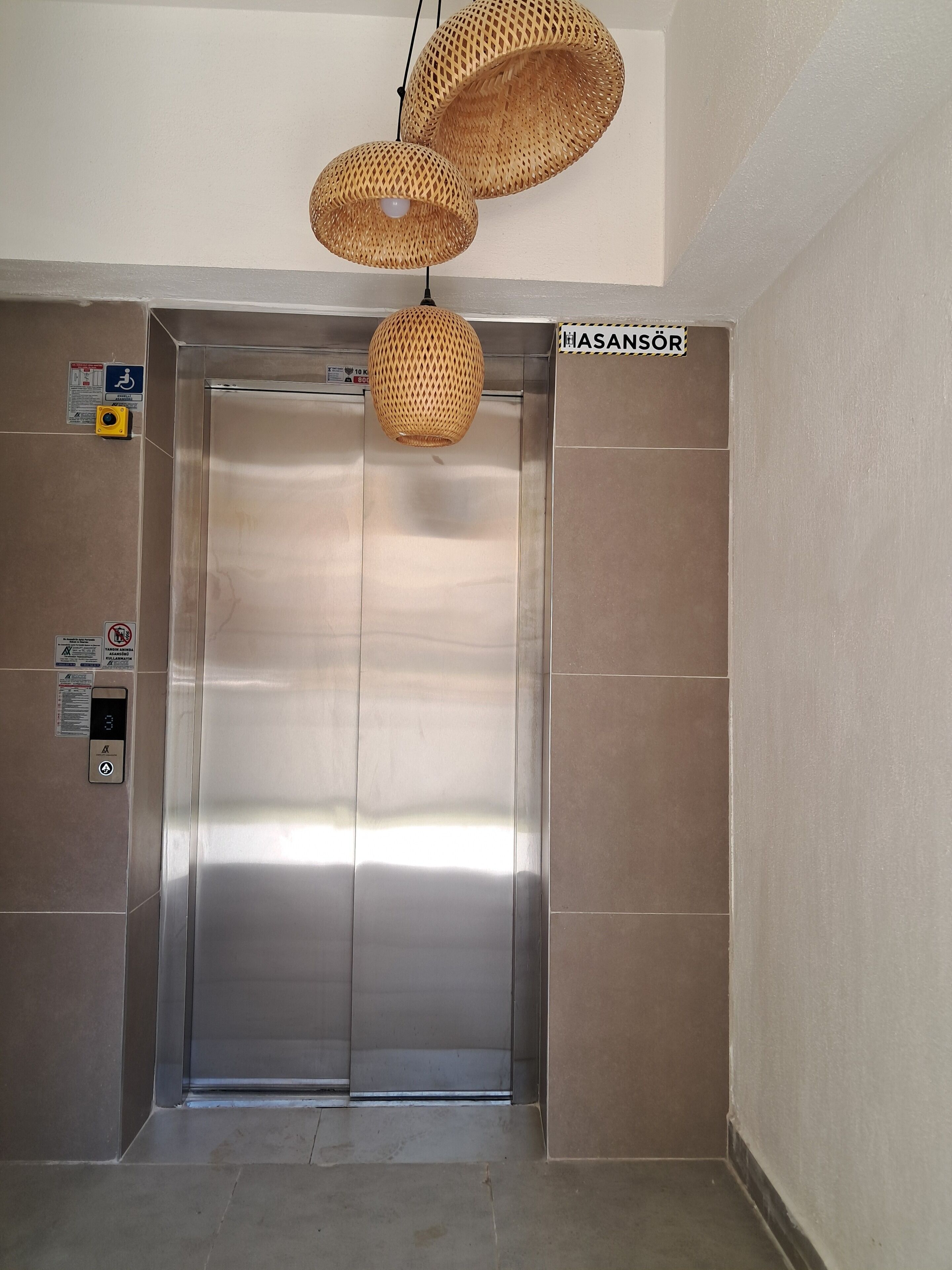 Um elevador com visor digital, sinal de acessibilidade para cadeiras de rodas e indicação da direção.