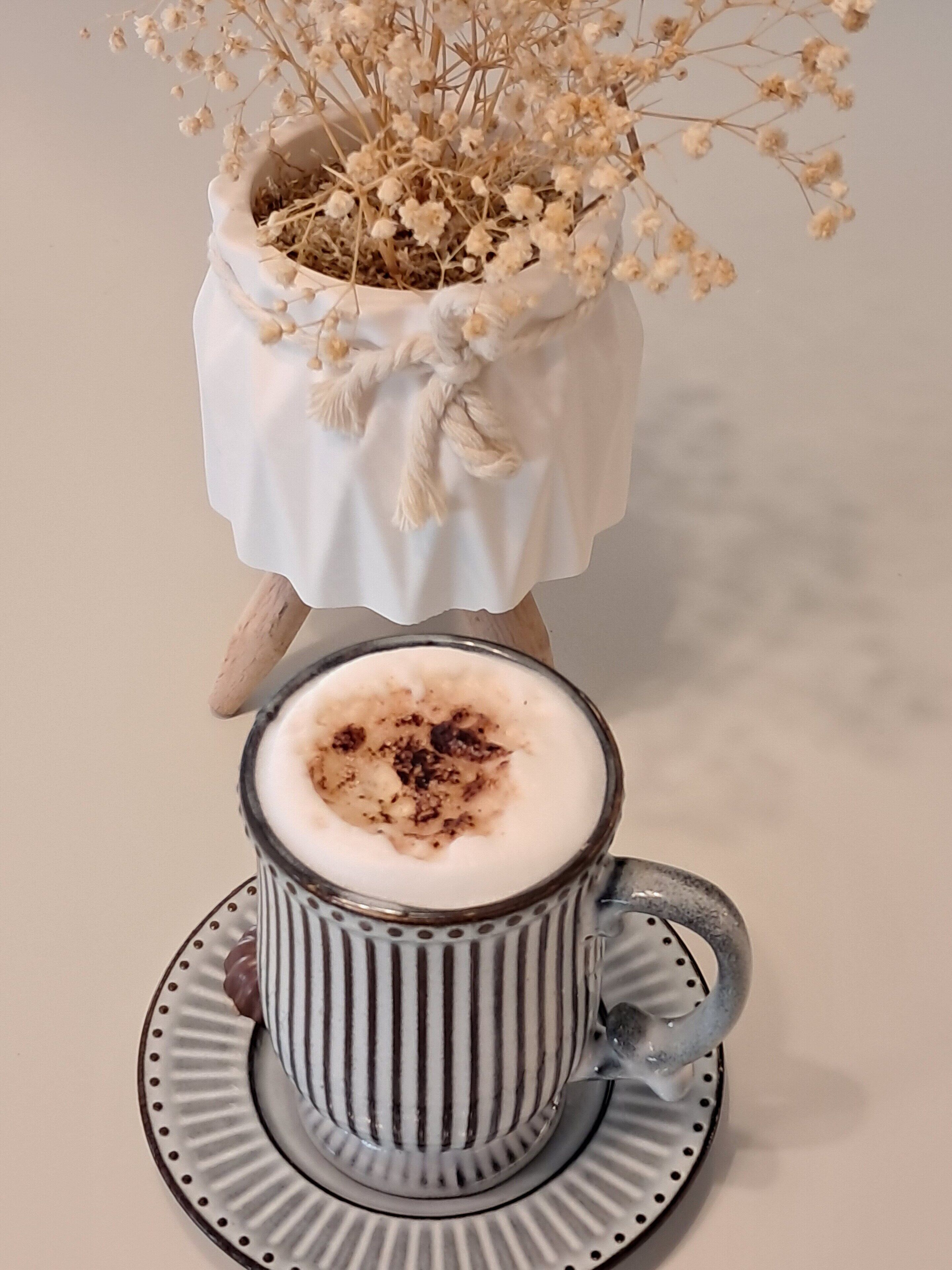 Een kop koffie met een schuimige laag en een beetje kaneel op een gestreept schoteltje.