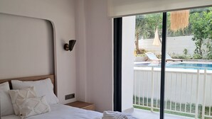 Ein modernes Schlafzimmer mit einem großen Bett, einem Nachttisch, einer Wandlampe und Blick auf ein Schwimmbad und eine Außenanlage durch eine Schiebetür.