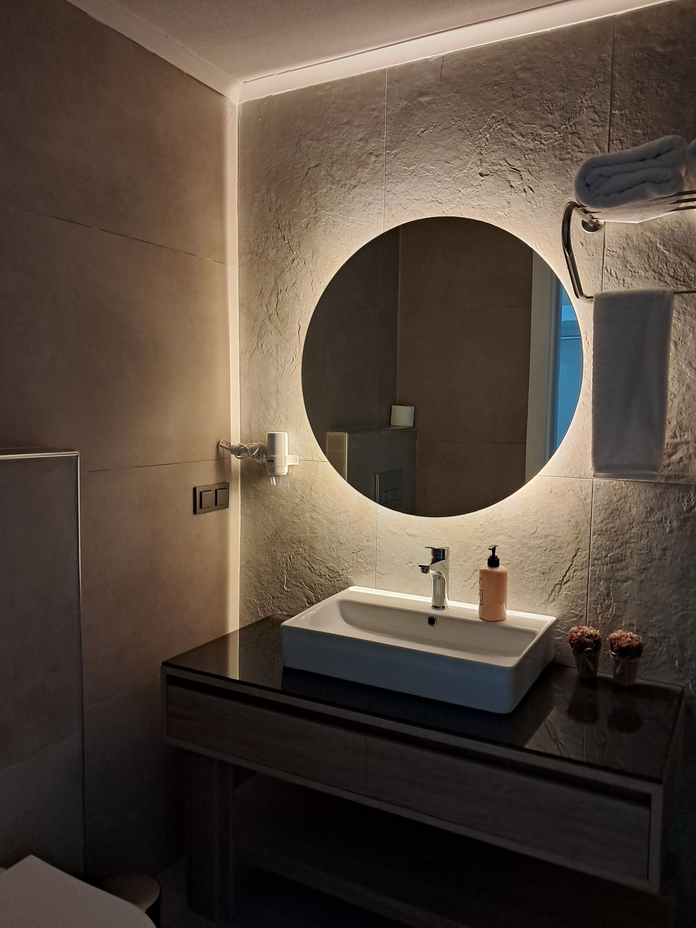 A modern bathroom with a round mirror, a white sink, and a dark countertop.