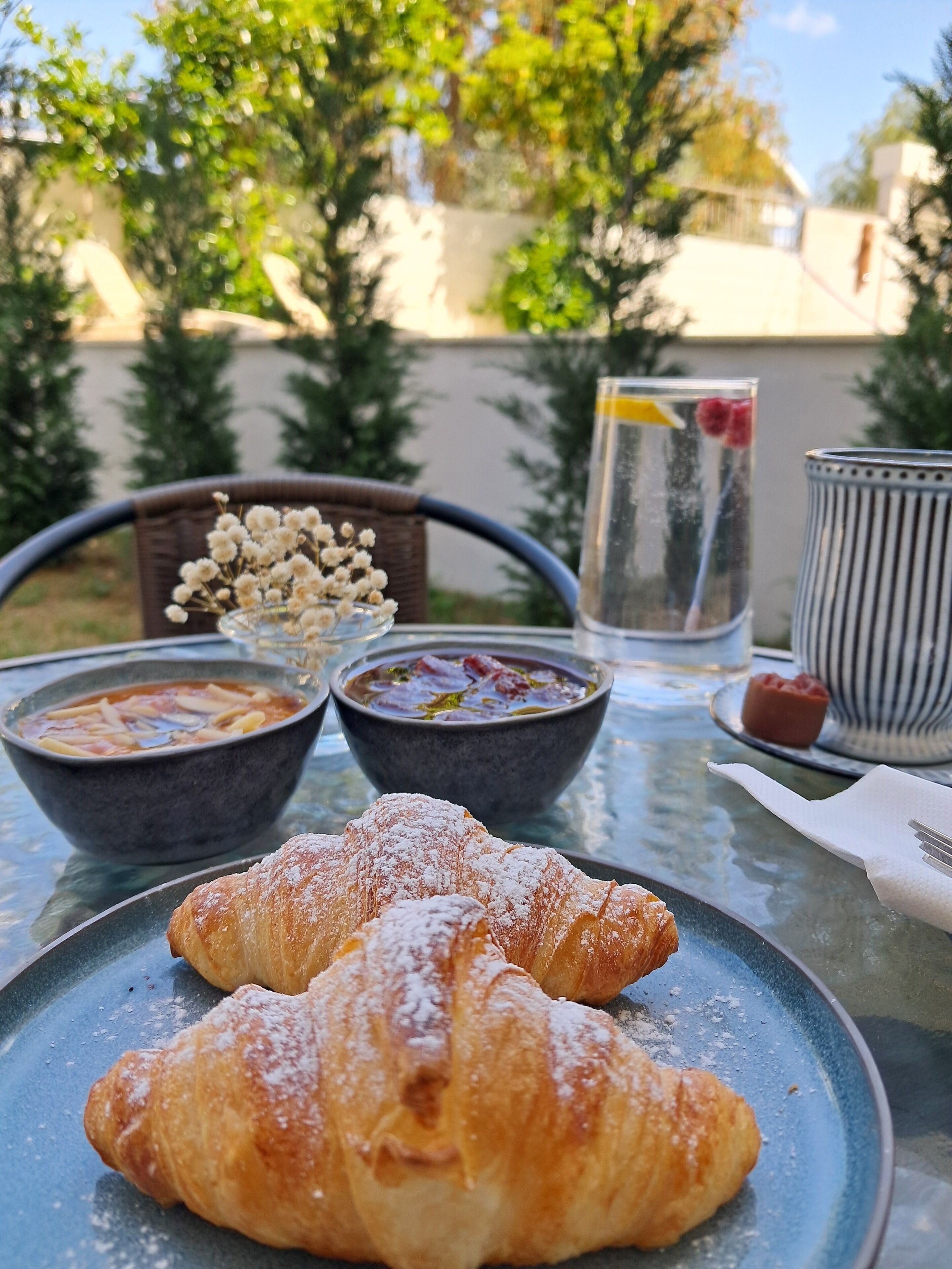 Uma mesa com um prato de croissants, duas tigelas de sopa e um copo de água com uma fatia de limão.