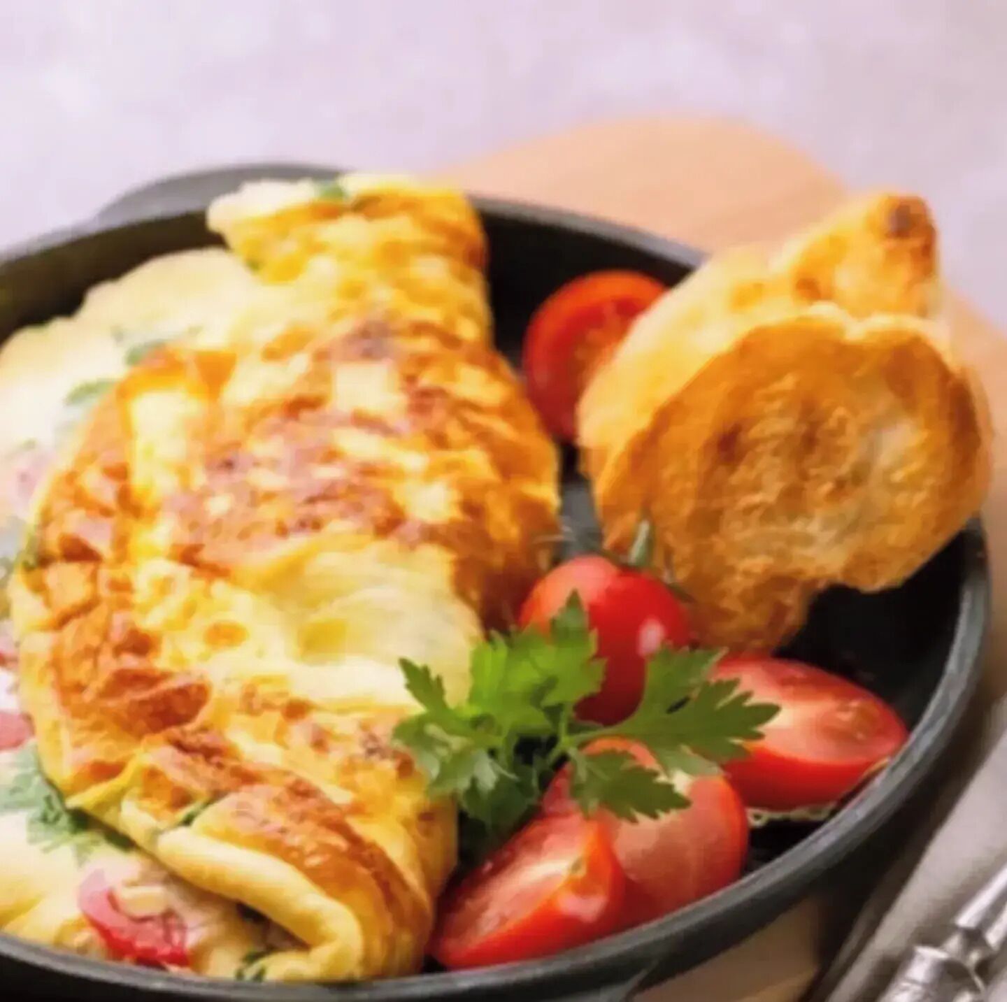 A breakfast plate with an omelette, a croissant, and cherry tomatoes.