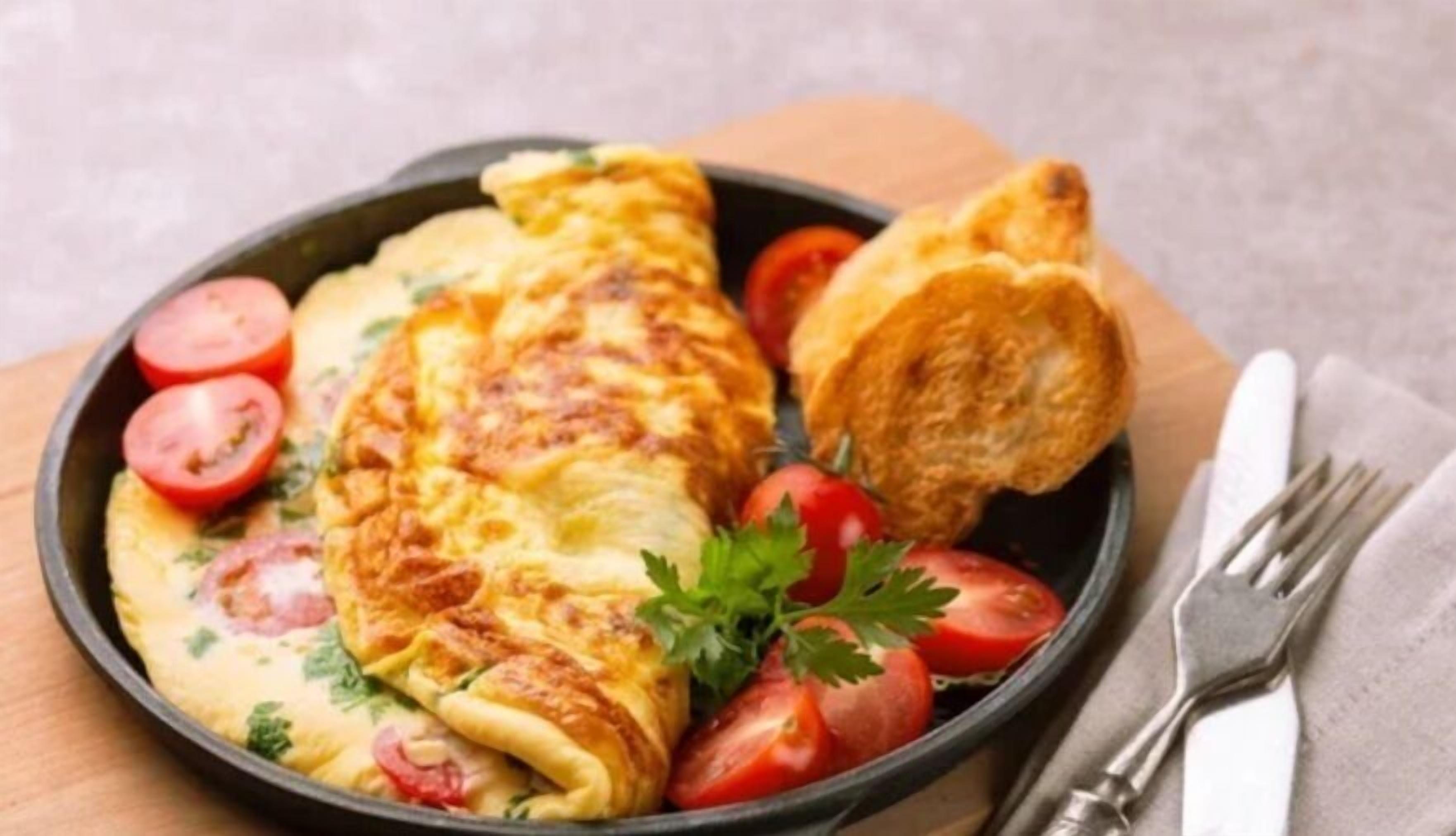 A breakfast plate with an omelette, tomatoes, parsley, and a piece of toast.