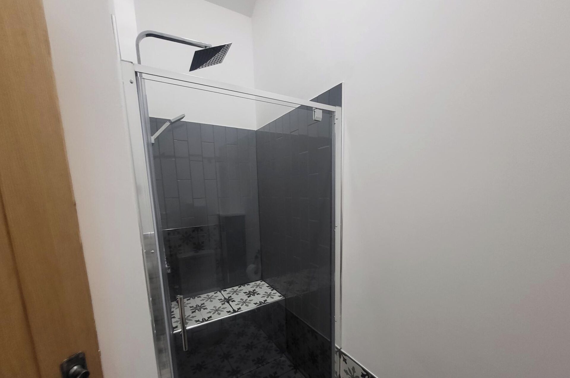 Una dutxa amb envidriament, un plat de dutxa i una porta que dona a una altra estança.
