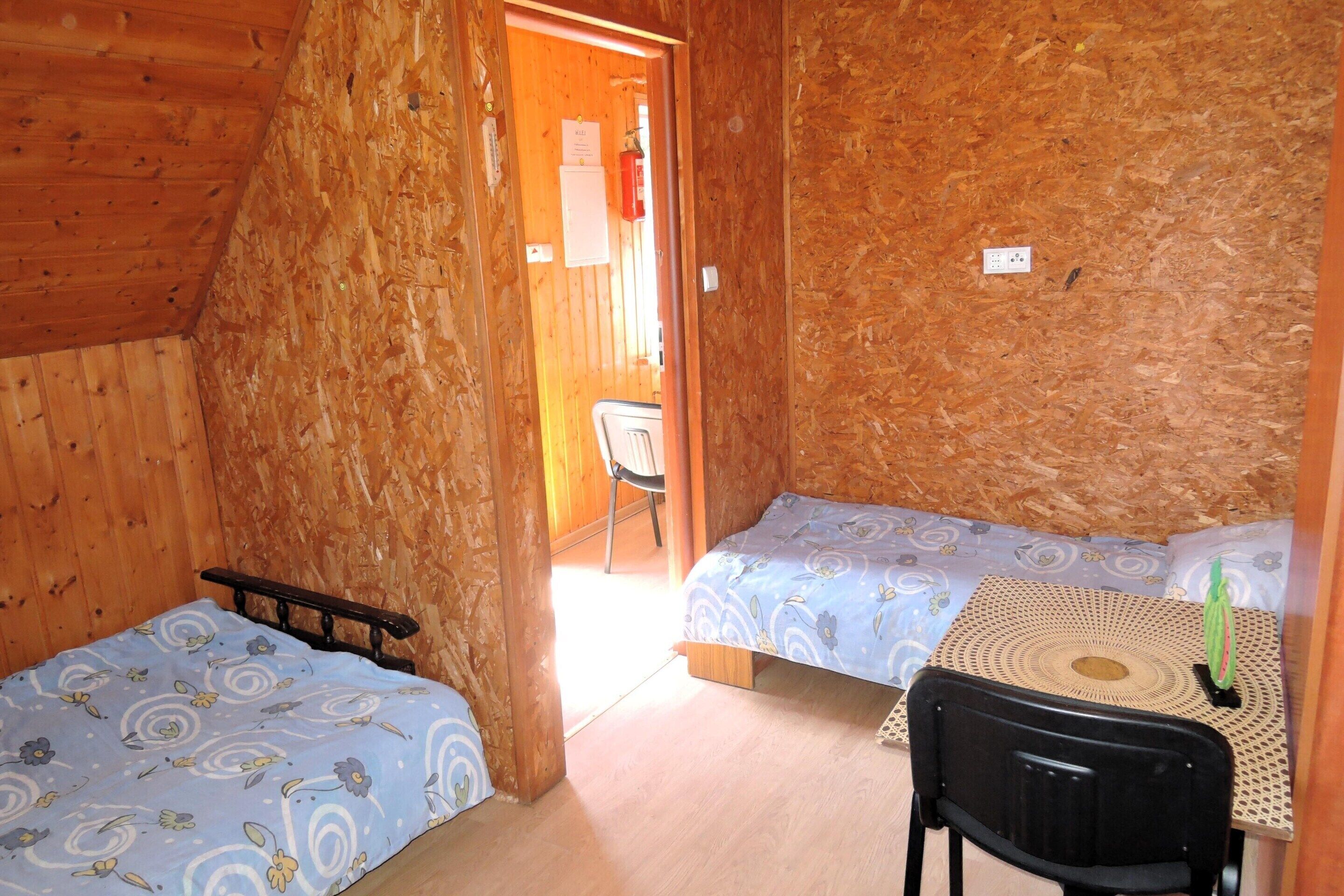A small, cozy room with two single beds, a wooden ceiling, and a small table with a chair.