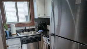 A compact kitchen with stainless steel appliances, white cabinets, and a wooden floor.