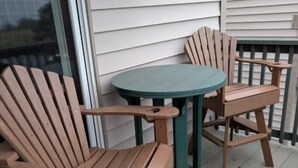 A wooden deck with two Adirondack chairs and a small round table.