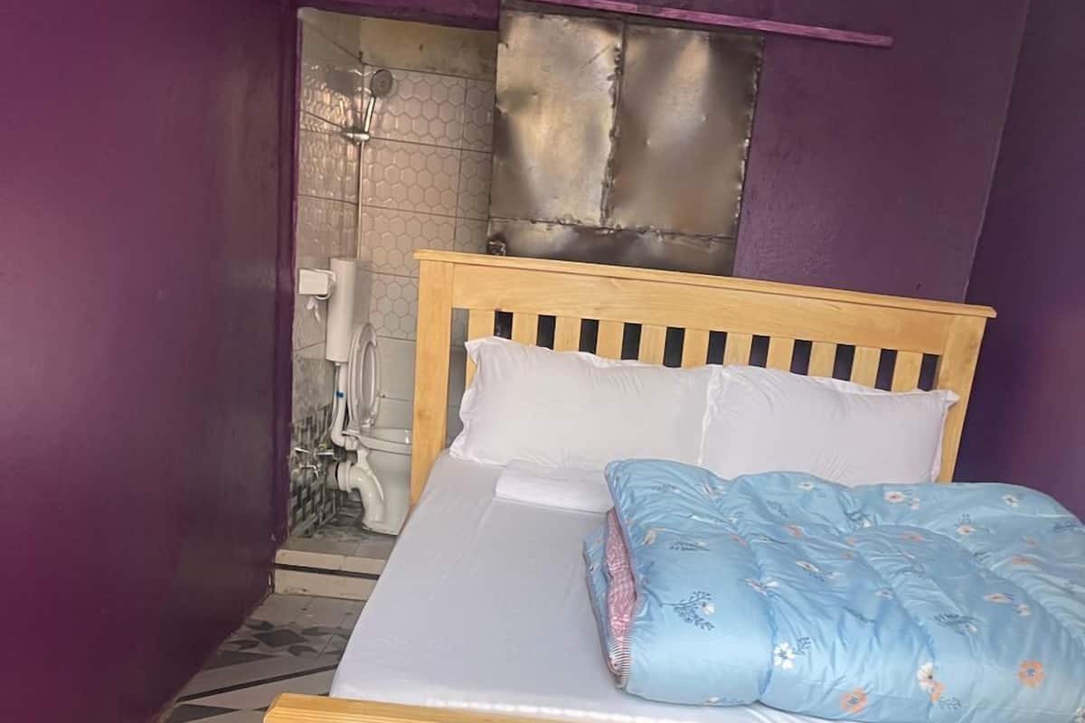 A single bed with a wooden frame and a blue floral bedspread in a room with purple walls and a tiled floor.