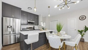 A modern kitchen with grey cabinets, stainless steel appliances, and a central island with white bar stools. - Homely Haven (Fort Worth)