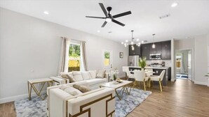 A modern living room with a sectional sofa, a dining area with a table and chairs, a kitchen in the background, and a ceiling fan. - Homely Haven (Fort Worth)