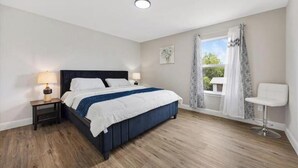 A bedroom with a bed, bedside tables, a window with curtains, and a chair. - Homely Haven (Fort Worth)