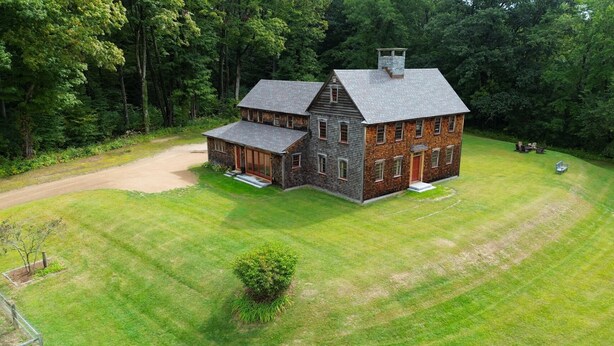 A large, two-story house with a stone foundation and a grey roof, surrounded by a well-maintained lawn and dense forest. - Copper Kettle Farm - newly renovated farmhouse with spectacular views (Sheffield)