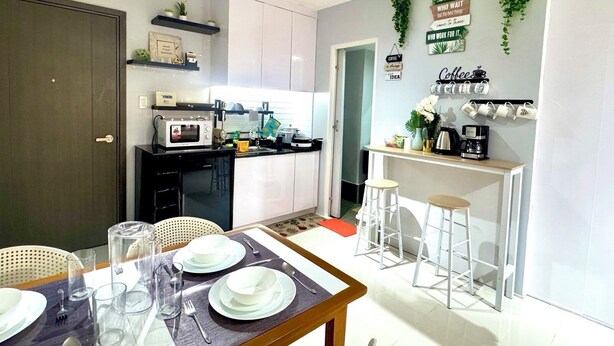 A compact kitchen with a dining area, white cabinets, a microwave, a coffee machine, and a wall-mounted plant. - Gorgeous Modern Condo in Bacolod City (Bacolod)