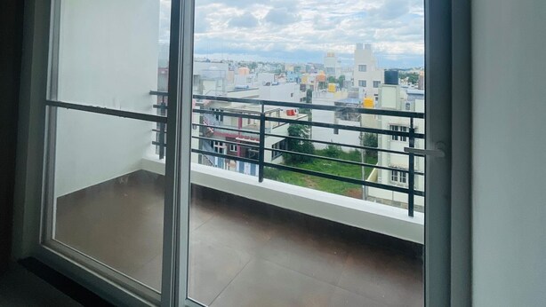 En balkong med ett metallräcke, utsikt över en stadsbild med byggnader och en molnig himmel.