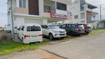 Un edificio moderno de apartamentos con un letrero que indica que es un 'West Service Apartment'. Hay varios coches estacionados en la parte delantera, y el edificio tiene un techo plano con un balcón en el piso superior.