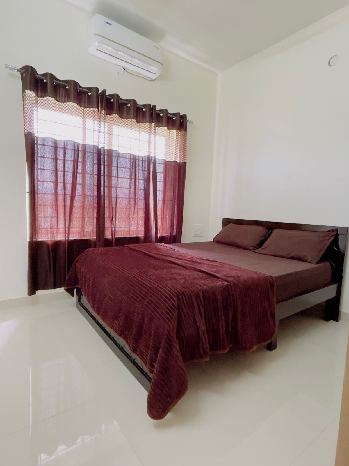 Un dormitorio con cama, ventana con cortinas y equipo de aire acondicionado.