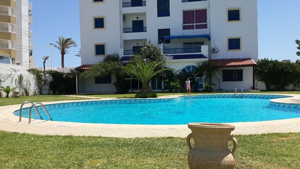 A swimming pool surrounded by a well-maintained lawn and a building with multiple balconies. - Apartment in Hammamet nord sea and mountain view (Nabeul‎)