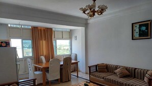 A living room with a sofa, a coffee table, and a dining area with a table and chairs. - Apartment in Hammamet nord sea and mountain view (Nabeul‎)