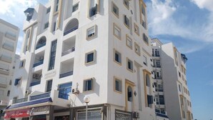A multi-story building with balconies, a storefront with a sign, and parked cars. - Apartment in Hammamet nord sea and mountain view (Nabeul‎)