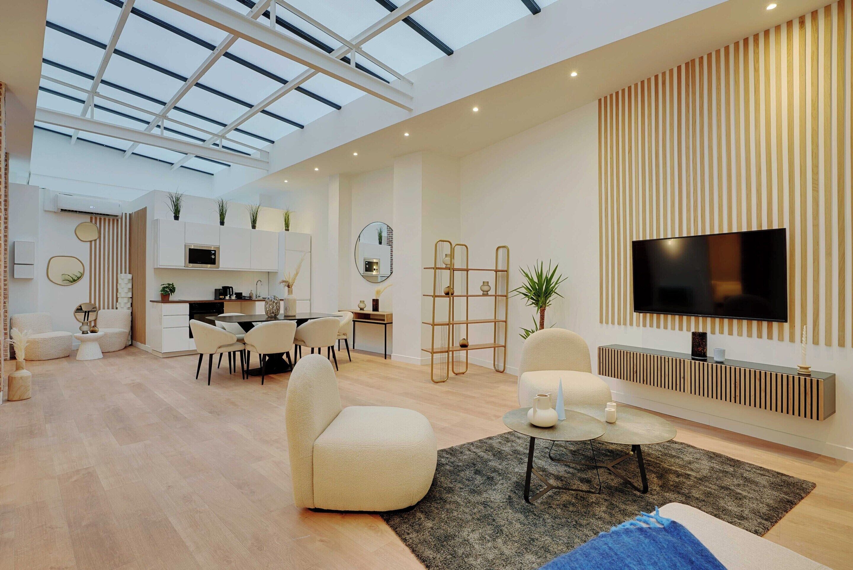 A modern living room with a flat-screen TV, comfortable seating, a dining area, and a kitchen.