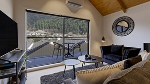 A modern living room with a large sliding glass door leading to a balcony, a TV, a sofa, and a coffee table. - Central Queenstown Apt 13a - walk to town (Queenstown)