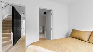 Un dormitorio con una cama, un tapete blanco mullido y una escalera que lleva a otra habitación.