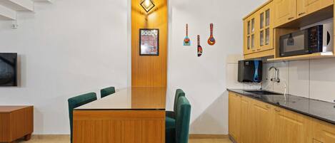 A modern kitchen with wooden cabinets, a microwave, and a dining area with a wooden table and green chairs.
