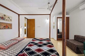 A bedroom with a bed, a wooden door, a ceiling fan, and a sofa. - Goan Hideaway - Cuatro (Arpora)