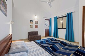 A bedroom with a bed, a chair, a ceiling fan, a window with curtains, and wall-mounted lights. - Goan Hideaway - Cuatro (Arpora)