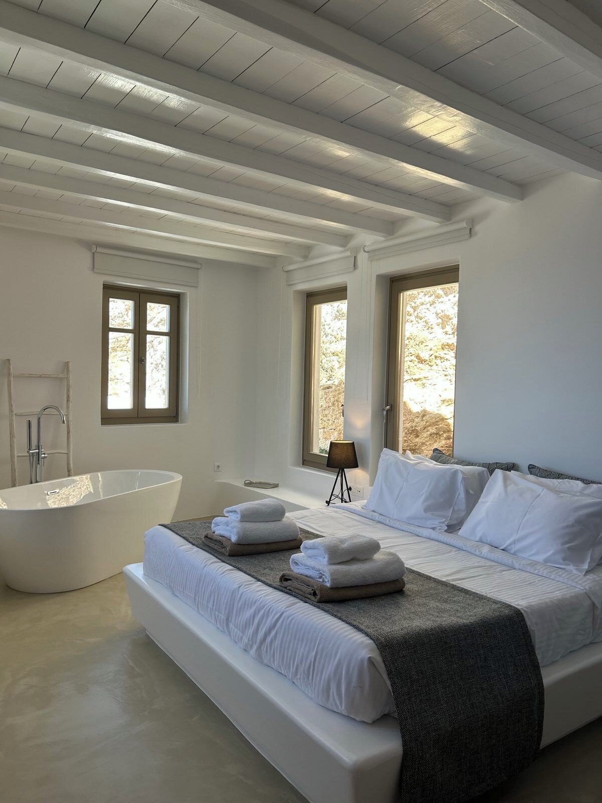 Un dormitorio moderno con una cama grande, una bañera y dos ventanas que ofrecen luz natural.