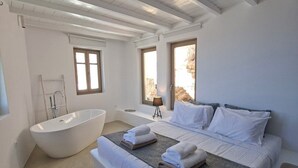 A modern bedroom with a large bed, a bathtub, and a view of the outdoors. - ANDELIAS SIGNATURE SUITES  (Folegandros)