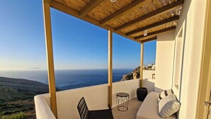 A balcony with a view of the sea, a sofa, a chair, and a small table. - ANDELIAS SIGNATURE SUITES  (Folegandros)