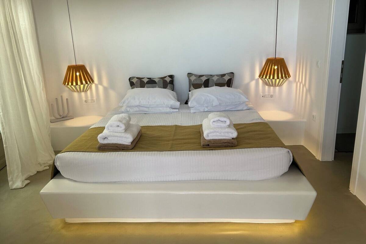 Moderni hotellihuone, jossa on suuri sänky, kaksi yöpöytävalaisinta ja siististi pedattu sänky, jossa on myös pyyhkeet.