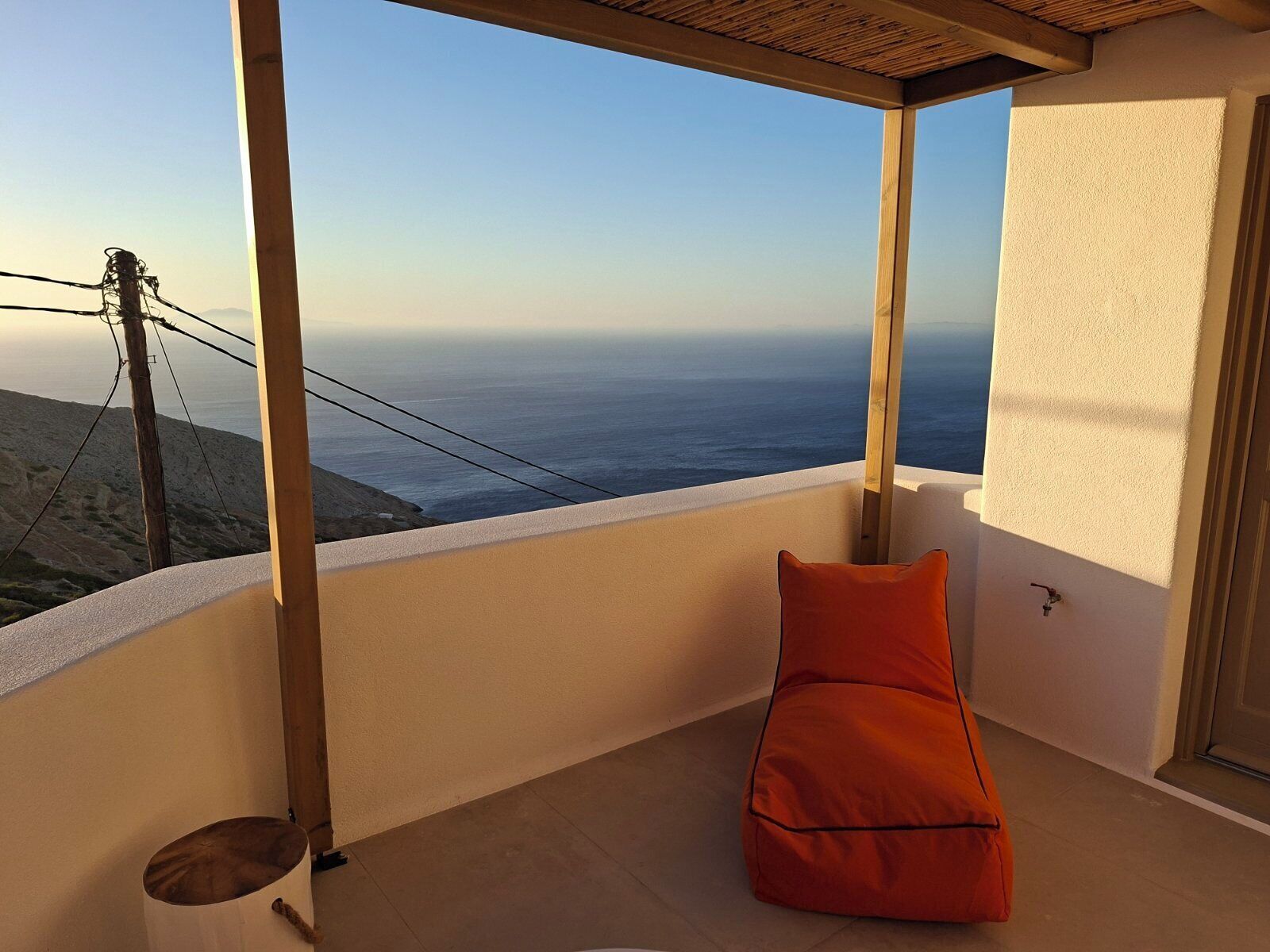 Un balcón con vista al mar, una viga de madera y un cojín naranja.