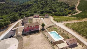 A villa with a swimming pool, surrounded by vineyards and a hilly landscape.