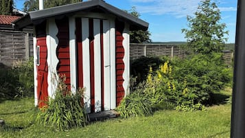 A small, red and white striped shed in a grassy yard with a wooden fence and trees in the background.