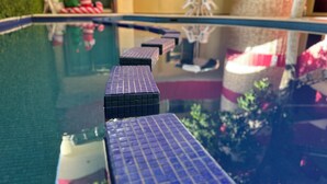 Une piscine dont le bord est recouvert de carreaux, et qui reflète un bâtiment décoré d’un sapin de Noël et surmonté d’une chaise.