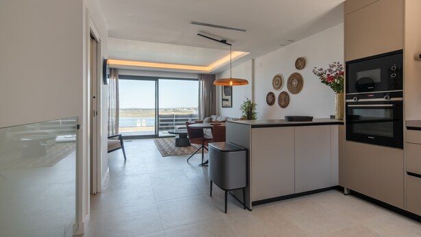 A modern kitchen with a built-in oven, a dining area with a sofa and chairs, and a large window offering a view of the outdoors.