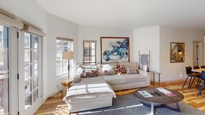 A spacious living room with a large sofa, a coffee table, and a dining area with chairs. - Westermere 211 - The Pinecone (Mountain Village)