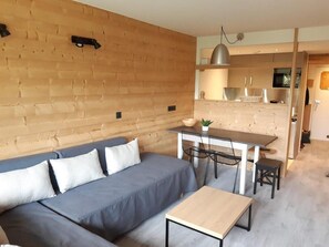 Uma sala de estar moderna com sofá, mesa de jantar e cadeiras. Há uma área de cozinha com armários e micro-ondas.
