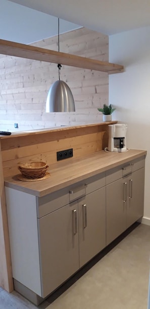 Cozinha moderna com bancada de madeira, cafeteira e luminária pendente.