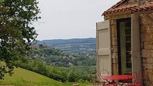 Ein rustikales Steinhaus mit einem roten Tisch und Stühlen vor der Fassade, mit Blick auf ein üppiges Tal.
