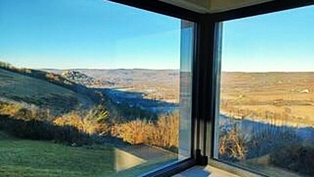 Ein Zimmer mit großem Fenster und Blick auf eine hügelige Landschaft.